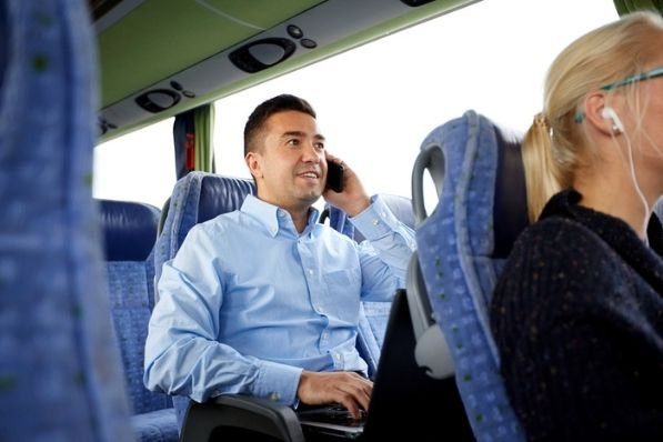 professional man talks on phone and works on computer while on a charter bus