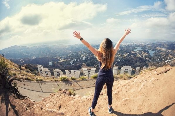 woman stands in front of hollywood sign in los angeles